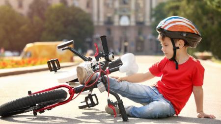 Ein Junge liegt neben einem Kinderfahrrad. Er trägt einen roten Fahrradhelm, ein rotes T-Shirt und eine Jeans. 