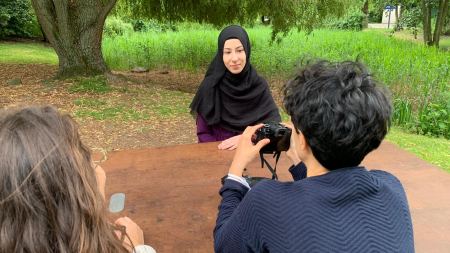 Junge Frau mit Kopftuch wird von zwei Frauen interviewt und gefilmt
