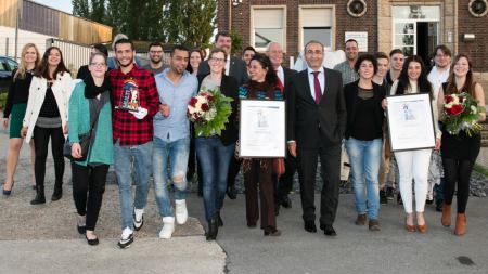 Mitglieder des Vereins Projekt Ankommen mit Pokal und Urkunde des Multi-Kulti-Preises 2016 sowie Kenan Küçük und Mitarbeitenden des Multikulturellen Forums vor der Hammer Geschäftsstelle laufen auf die Kamera zu