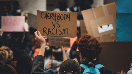 Demonstrierende von hinten, gut lesbar ein Schild mit der Aufschrift "Everybody vs. Racism"