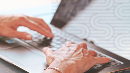 Hände tippen auf die Tastatur eines aufgeklappten Laptops