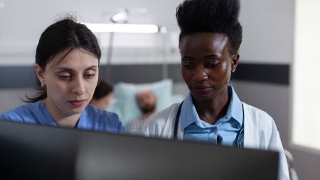 Pflegekraft und Ärztin blicken auf Bildschirm in Patient*innenzimmer