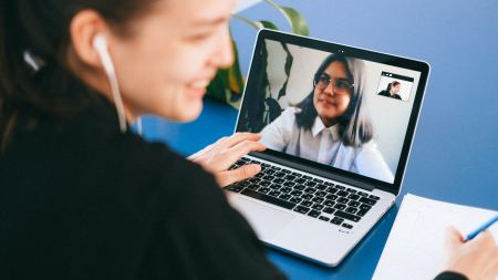 Frau sitzt vor Laptop mit Videokonferenz-App