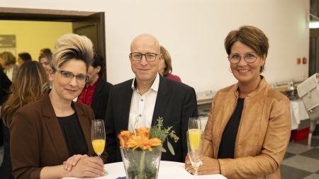 Zwei Frauen und ein Mann lächeln in die Kamera.