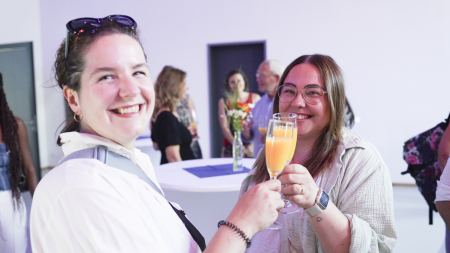Zwei Frauen lächeln in die Kamera und stoßen mit Gläsern an