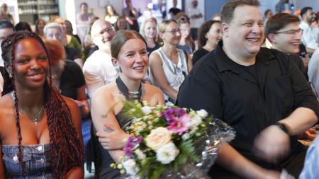 Nahaufnahme von drei Personen mit Blumenstrauß im Publikum