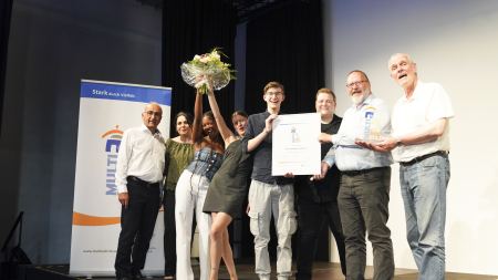 Gruppe mit Urkunde und Blumenstrauß auf Bühne