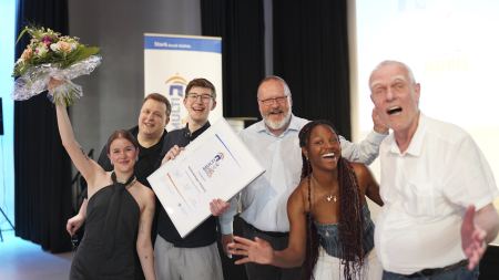 Zwei Frauen und vier Männer freuen sich mit Pokal und Blumenstrauß und lachen in die Kamera