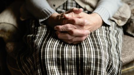 ältere Person sitzt mit gefalteten Händen