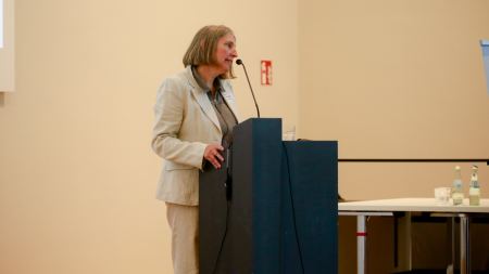 Frau steht an einem Rednerpult und spricht in ein Mikrofon.