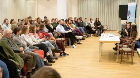 Zwei Personen sitzen vor Publikum in einem hellen Raum