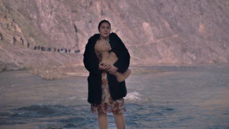 Frau vor Berg-See-Kulisse mit schwarzem Mantel und Schaufensterpuppenoberkörper
