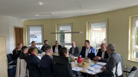 Menschen sitzen um einen Konferenztisch, auf dem belegte Brötchen und Kaffeetassen stehen