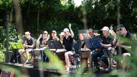 Mehrere Musiker*innen sitzen auf einer Bühne und halten unterschiedliche Instrumente.