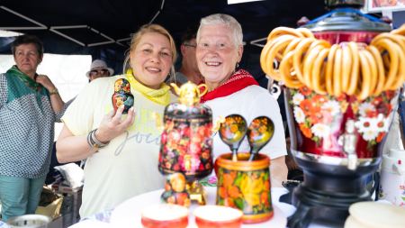 Zwei Frauen lächeln in die Kamera. Vor ihnen steht ukrainisch-russisch traditionell bemaltes Holzgeschirr auf einem Tisch. 
