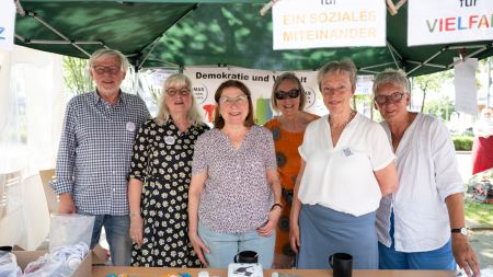 Sechs Personen stehen nebeneinander in einem Pavillon und lächeln. 