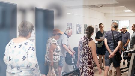 Menschen gehen durch einen Flur. An den Wänden hängen Fotos. 
