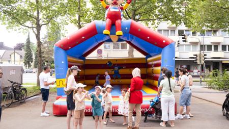Vor einer bunten Hüpfburg stehen zahlreiche Kinder und Erwachsene.