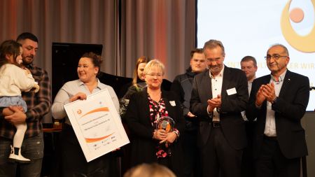 Preisträgerteam mit Urkunde und Pokal steht auf der Bühne