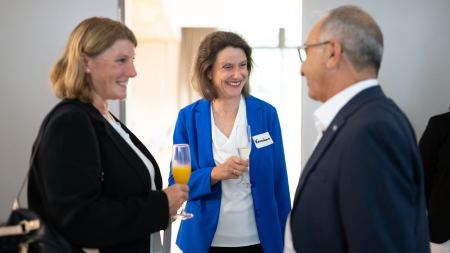 Zwei Frauen mit Blazer und ein Mann mit Jackett stehen sich gegenüber.