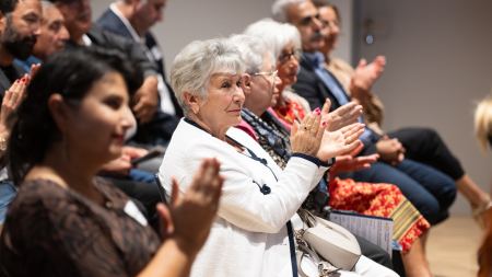 Applaudierendes Publikum sitzt in einem Saal auf Stuhlreihen.