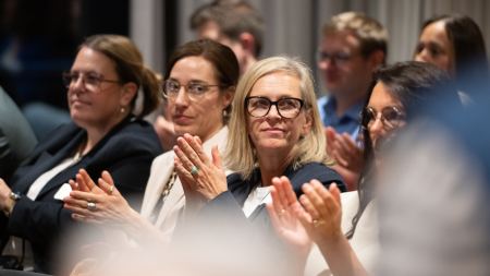 Applaudierendes Publikum sitzt auf Stuhlreihen in einem Saal. 
