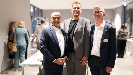 Drei Männer in Anzügen stehen für ein Foto nebeneinander.