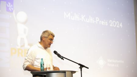Mann steht am Rednerpult auf Bühne