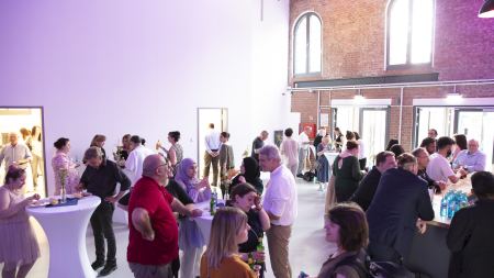 Menschen stehen in einem feierlich erleuchteten Raum zwischen Stehtischen