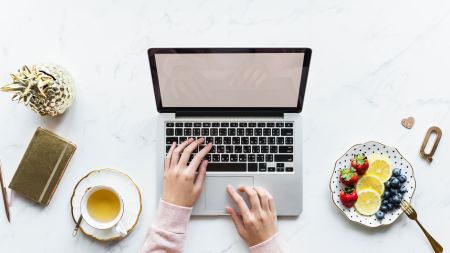 Laptop, Tee, Teller mit Früchten auf Schreibtisch