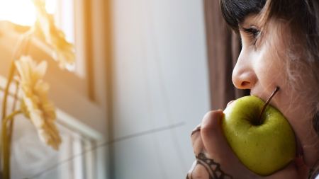 Frau mit Henna an der Hand isst grünen Apfel und schaut aus Fenster