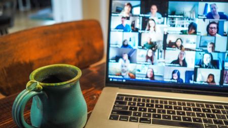 Laptop neben Kaffeetasse, aufgeklappt und in mit anderen Menschen in einer Online-Konferenz verbunden