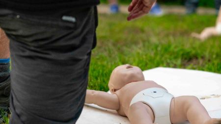 Ein Erwachsener kniet vor einer Erste Hilfe-Übungspuppe. 