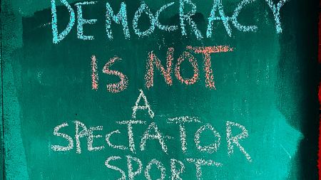 Kreidetext auf grünem Hintergrund "Democracy is not a spectator sport"