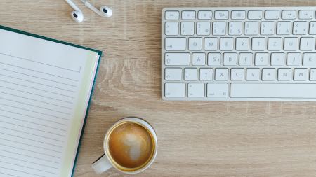 Schreibtisch mit Tastatur, Notizblock, Kopfhörer und Kaffeetasse