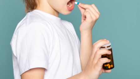 Ein Kind hält eine Tablette vor sein Gesicht und öffnet den Mund.