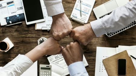 vier Personen geben sich über einem Schreibtisch die Hand