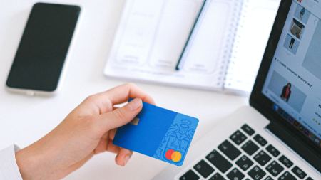 Hand hält Bankkarte vor aufgeklapptem Laptop