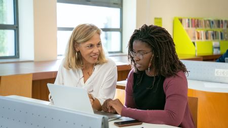 Frau arbeitet am Laptop und erhält Unterstützung durch eine weitere Frau Frau arbeitet am Laptop und erhält Unterstützung durch eine weitere Frau