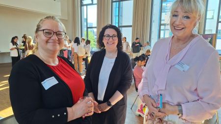 Drei Frauen stehen nebeneinander und lächeln in die Kamera.