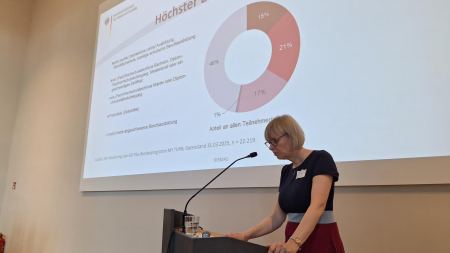 Eine Frau steht an einem Rednerpult und spricht in ein Mikrofon.