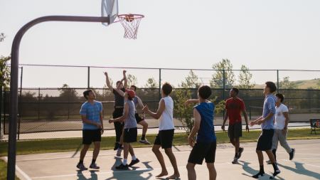 Jugendliche spielen draußen auf einem Basketballfeld Basketball