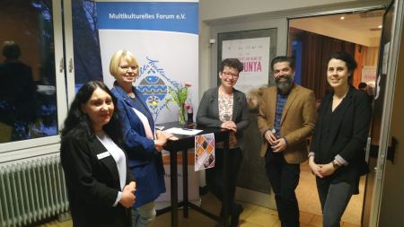 Vier Frauen und ein Mann an Stehtisch vor Banner „Multikulturelles Forum"