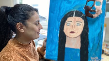 Frau blickt Selbstportrait auf blauer Leinwand an