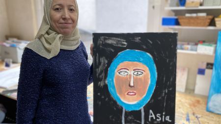 Frau neben ihrem Selbstportrait auf schwarzer Leinwand