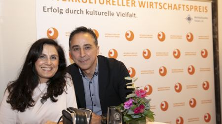 Frau und Mann posieren vor Fotowand "Interkultureller Wirtschaftspreis"