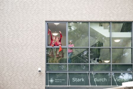 Zwei Frauen winken aus einem Fenster einer oberen Etage. Sie tragen traditioneller Gewänder.