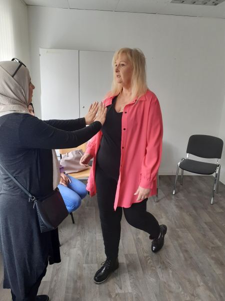 Zwei Frauen stehen sich gegenüber. Eine der Frauen streckt ihre Arme der anderen Frau entgegen. 