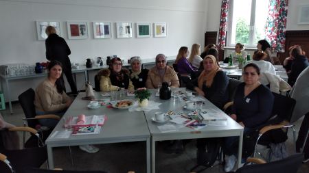 Die Teilnehmerinnen des Frauencafés freuen sich über Informationen zu Unterstützungsmöglichkeiten. Viele Frauen sitzen um einen Tisch herum und blicken in die Kamera.