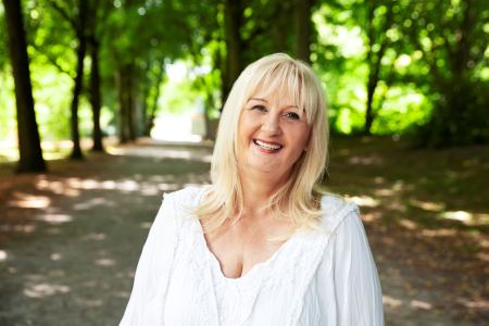 Simona Clemens: Blonde Frau mit weißem Oberteil vor Laubbäumen
